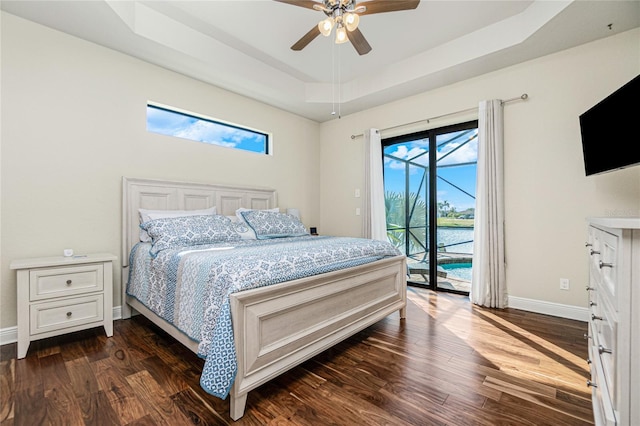 bedroom with dark hardwood / wood-style floors, access to exterior, ceiling fan, a raised ceiling, and a water view