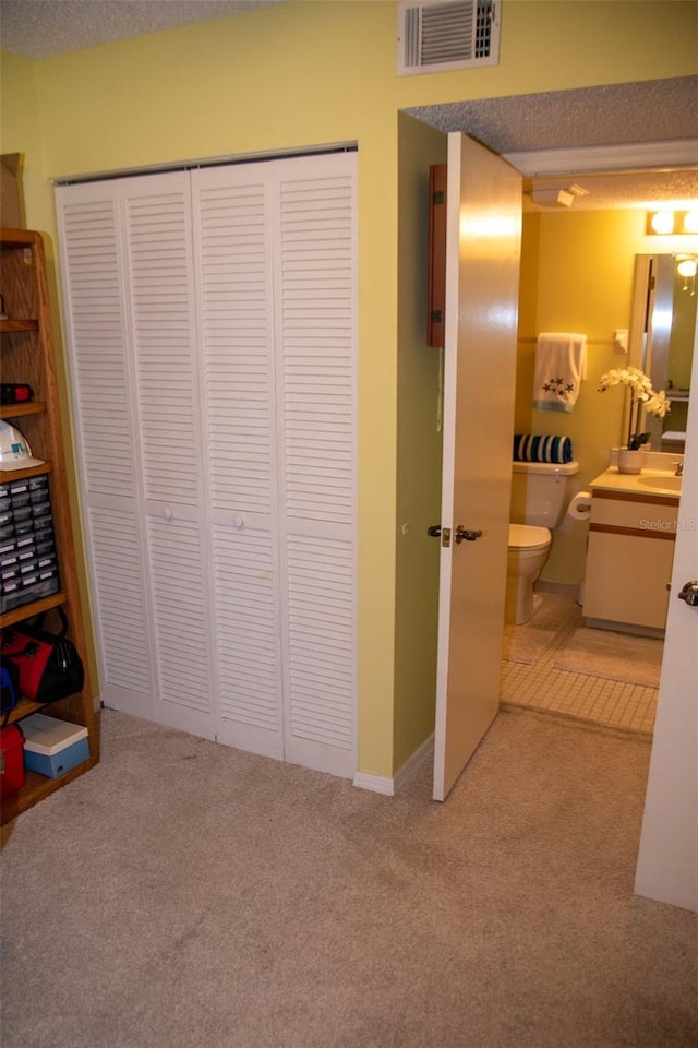 bedroom with ensuite bathroom, light colored carpet, a textured ceiling, and a closet