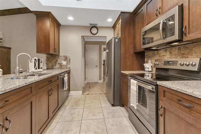 kitchen with backsplash, sink, stainless steel appliances, light tile floors, and light stone counters