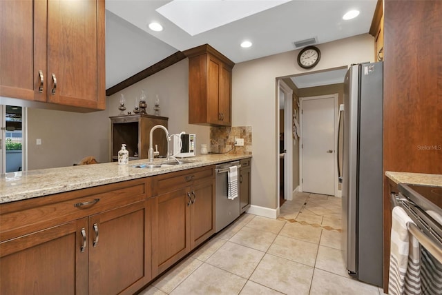 kitchen with appliances with stainless steel finishes, vaulted ceiling with skylight, sink, light tile floors, and light stone counters