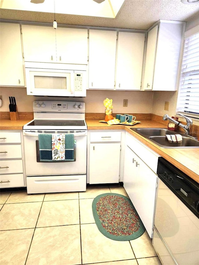 kitchen featuring a textured ceiling, white appliances, light tile patterned floors, sink, and white cabinetry