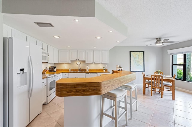 kitchen featuring sink, light tile patterned flooring, white appliances, a kitchen bar, and white cabinets