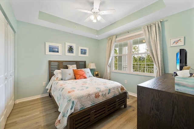 bedroom with a closet, a tray ceiling, light hardwood / wood-style flooring, and ceiling fan