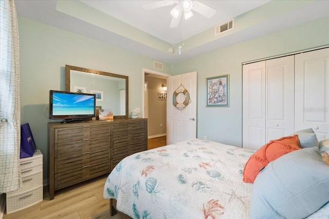 bedroom with ceiling fan, a raised ceiling, light hardwood / wood-style flooring, and a closet