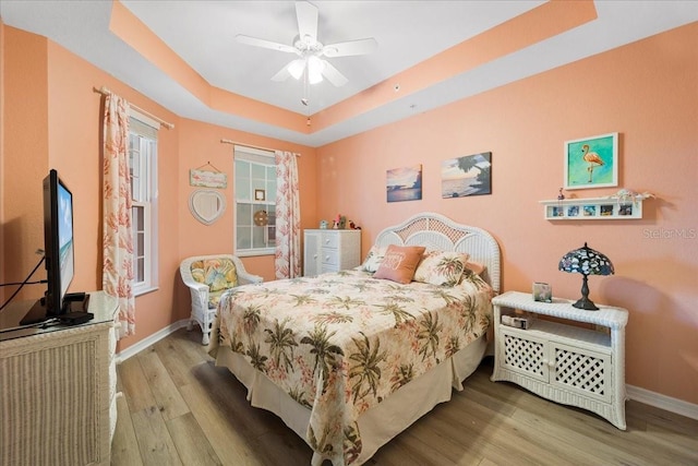 bedroom featuring hardwood / wood-style floors, a raised ceiling, and ceiling fan