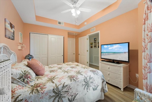 bedroom featuring a tray ceiling, ceiling fan, a closet, and light hardwood / wood-style floors