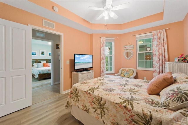 bedroom with a tray ceiling, ceiling fan, and light hardwood / wood-style floors