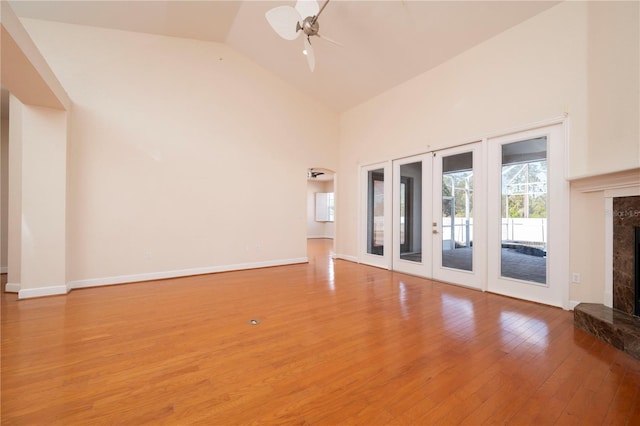 unfurnished living room featuring ceiling fan, hardwood / wood-style flooring, high vaulted ceiling, french doors, and a high end fireplace