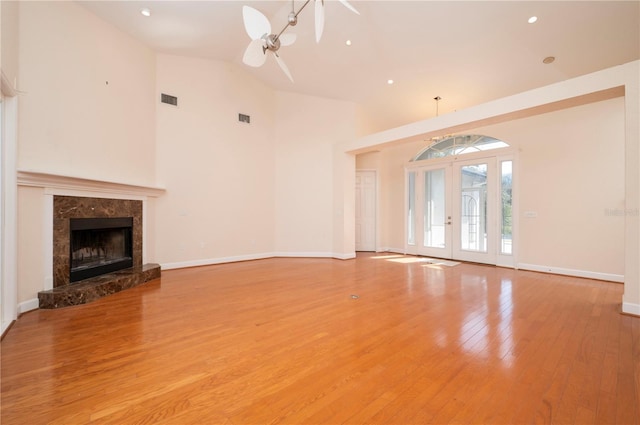 unfurnished living room featuring a premium fireplace, french doors, high vaulted ceiling, light wood-type flooring, and ceiling fan