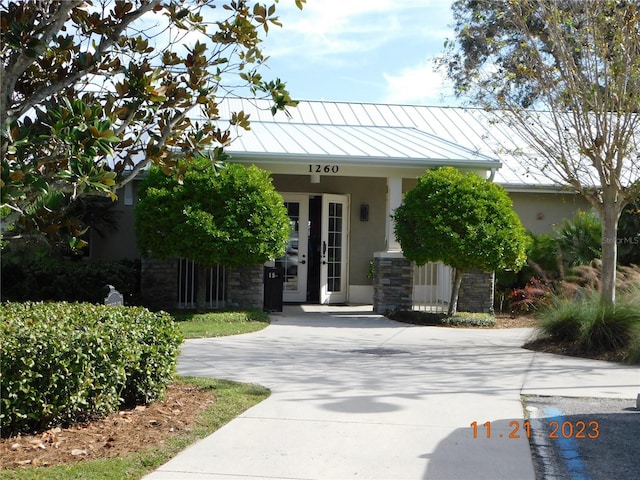 view of front of home featuring stucco siding, a standing seam roof, stone siding, french doors, and metal roof