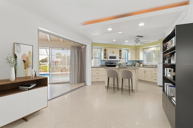 kitchen featuring a kitchen island, a breakfast bar, plenty of natural light, white appliances, and cream cabinetry