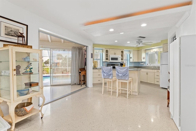 kitchen featuring a kitchen island, a breakfast bar, sink, ceiling fan, and white appliances