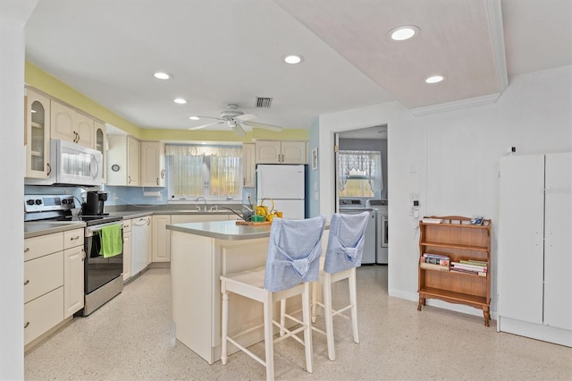 kitchen featuring sink, a center island, a kitchen breakfast bar, white appliances, and washing machine and dryer