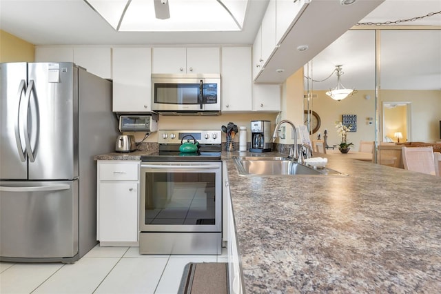 kitchen featuring light tile patterned floors, stainless steel appliances, a sink, white cabinetry, and dark countertops