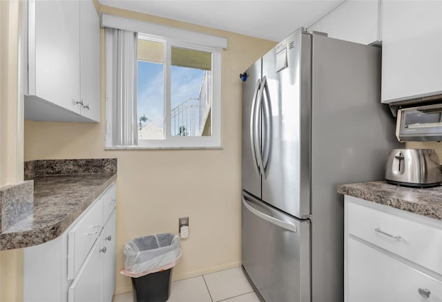 kitchen with stainless steel refrigerator, light tile patterned floors, and white cabinets