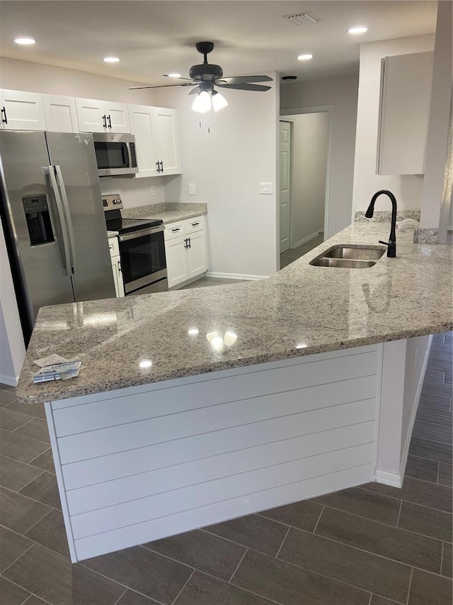 kitchen with stainless steel appliances, a peninsula, a sink, and white cabinetry