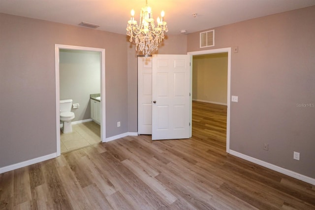 unfurnished bedroom featuring a notable chandelier, wood-type flooring, and ensuite bath