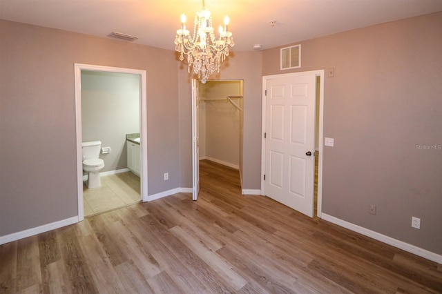 unfurnished bedroom with hardwood / wood-style floors, ensuite bathroom, a walk in closet, a chandelier, and a closet