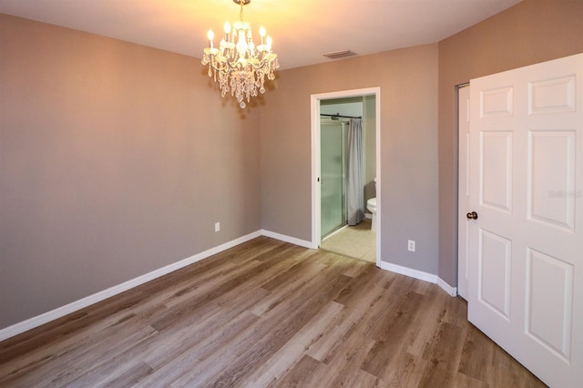 unfurnished bedroom featuring hardwood / wood-style flooring, a chandelier, and ensuite bath