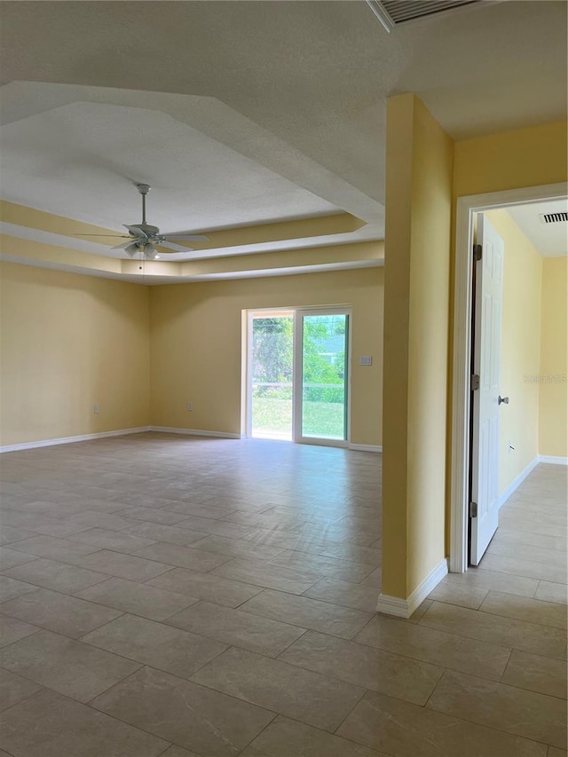 tiled spare room featuring ceiling fan and a tray ceiling