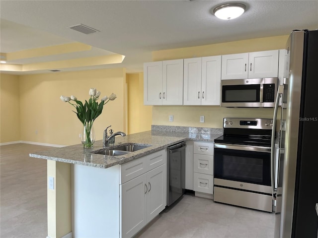 kitchen with sink, stainless steel appliances, light stone counters, white cabinets, and kitchen peninsula