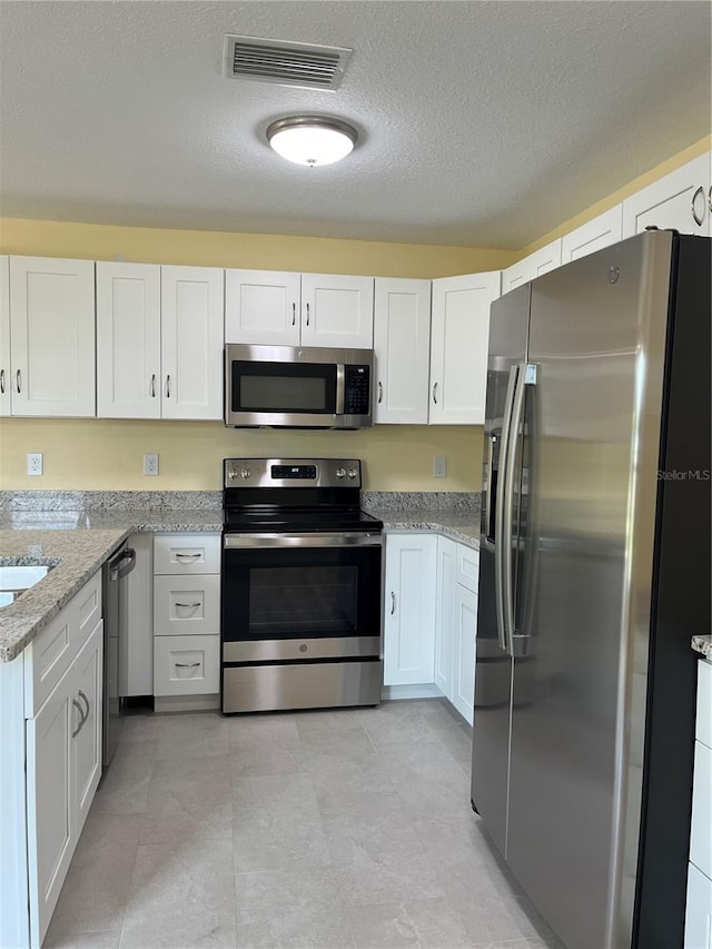 kitchen with light stone countertops, a textured ceiling, stainless steel appliances, and white cabinets