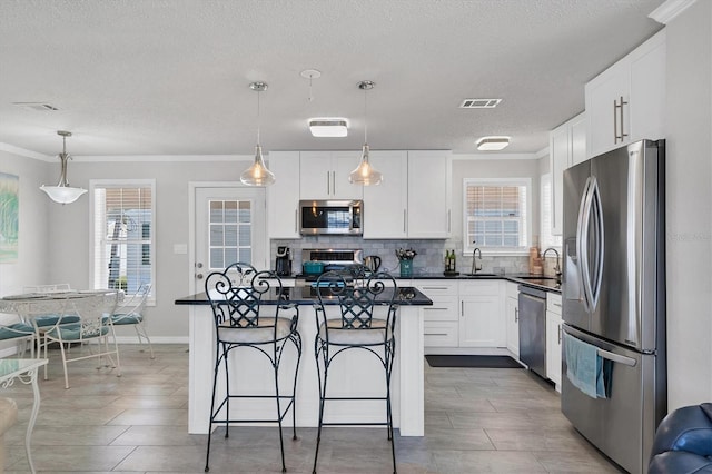 kitchen featuring hanging light fixtures, white cabinetry, a kitchen island, and appliances with stainless steel finishes