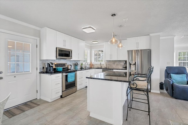 kitchen featuring white cabinetry, a breakfast bar, appliances with stainless steel finishes, hanging light fixtures, and a center island