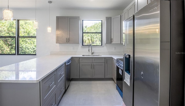 kitchen featuring light tile patterned flooring, kitchen peninsula, stainless steel appliances, pendant lighting, and sink