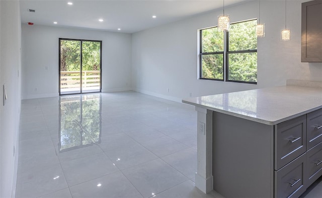 kitchen with light stone counters, gray cabinetry, decorative light fixtures, and light tile patterned floors