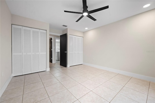 unfurnished bedroom with light tile patterned flooring, ceiling fan, and multiple closets