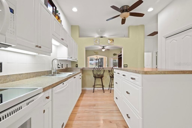 kitchen with backsplash, white appliances, sink, white cabinets, and light hardwood / wood-style floors