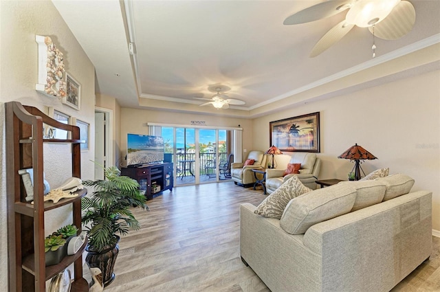 living room with crown molding, ceiling fan, a tray ceiling, and light wood-type flooring