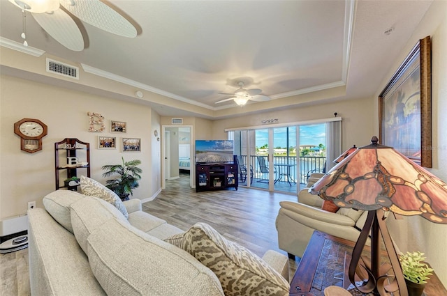 living room with a tray ceiling, ornamental molding, a baseboard heating unit, ceiling fan, and light hardwood / wood-style floors