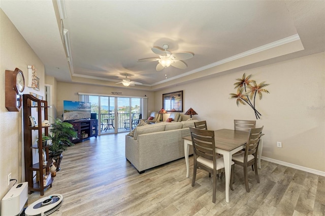 living room with ornamental molding, light hardwood / wood-style flooring, ceiling fan, and a tray ceiling