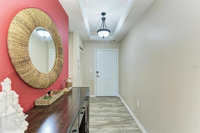 doorway to outside with crown molding, light hardwood / wood-style floors, and a raised ceiling