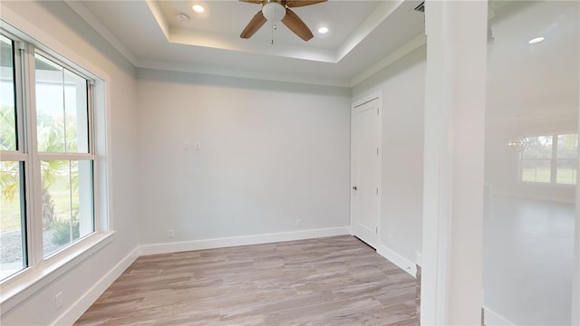 unfurnished room featuring a raised ceiling, crown molding, ceiling fan with notable chandelier, and light hardwood / wood-style flooring