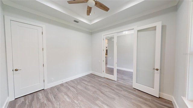 unfurnished bedroom featuring french doors, ceiling fan, light hardwood / wood-style floors, and a raised ceiling