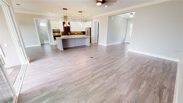 unfurnished living room featuring light wood-type flooring, ceiling fan, crown molding, and sink