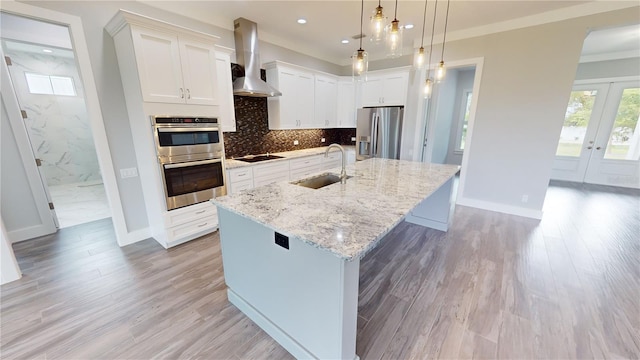 kitchen featuring a center island with sink, stainless steel appliances, hanging light fixtures, wall chimney range hood, and sink