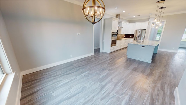 kitchen with white cabinets, decorative light fixtures, stainless steel appliances, an island with sink, and a chandelier