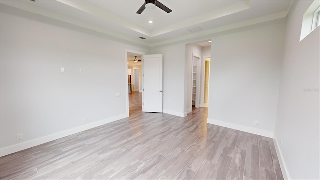 unfurnished bedroom featuring ceiling fan, light hardwood / wood-style floors, and a tray ceiling