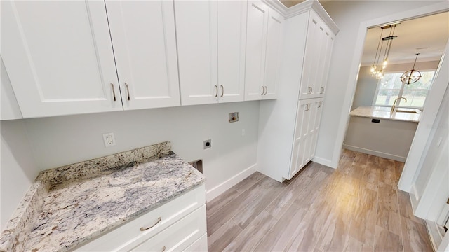 washroom with a notable chandelier, light hardwood / wood-style floors, washer hookup, hookup for an electric dryer, and cabinets