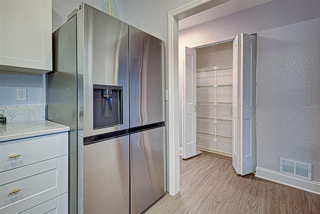 kitchen with stainless steel fridge with ice dispenser, light stone counters, and light hardwood / wood-style flooring