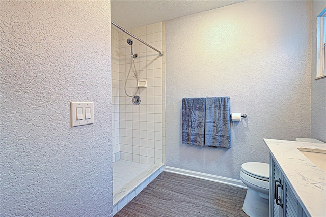 bathroom featuring toilet, a tile shower, hardwood / wood-style floors, a textured ceiling, and vanity