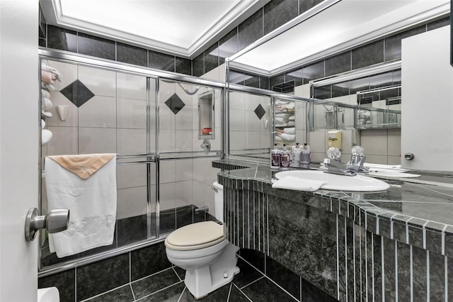 bathroom with sink, a shower with shower door, tile walls, and toilet