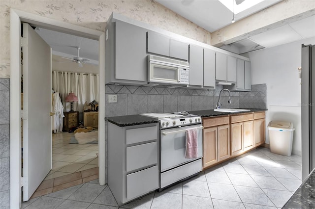 kitchen with ceiling fan, sink, dark stone counters, white appliances, and decorative backsplash