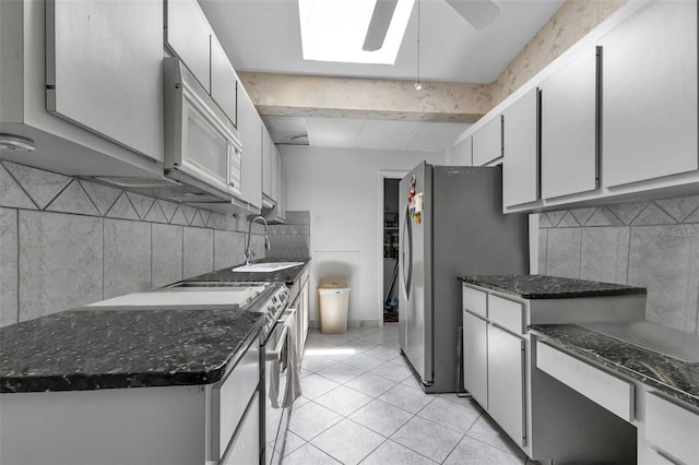 kitchen featuring appliances with stainless steel finishes, a skylight, ceiling fan, sink, and light tile patterned floors