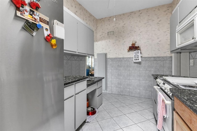 kitchen featuring light tile patterned floors, stainless steel appliances, tile walls, and dark stone countertops