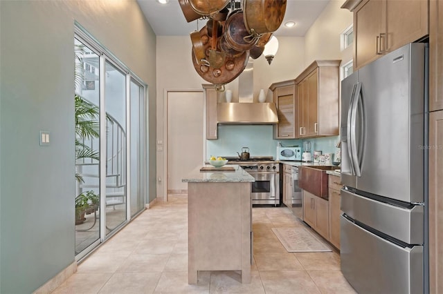 kitchen featuring a center island, appliances with stainless steel finishes, wall chimney range hood, light stone counters, and plenty of natural light